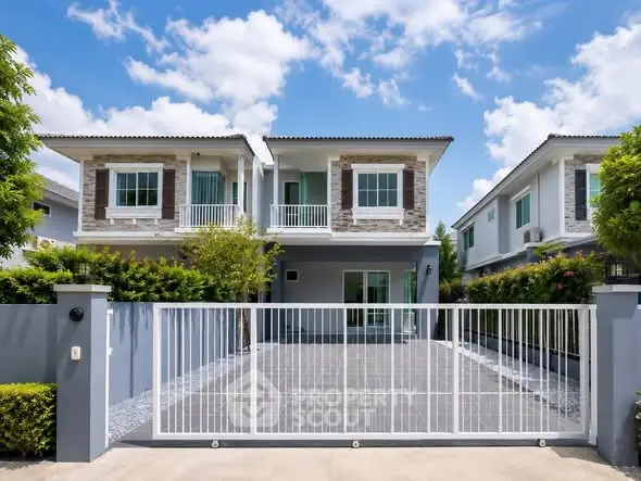Modern two-story house with gated driveway and lush greenery under a clear blue sky.