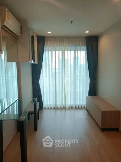 Modern living room with large window and wooden flooring in a high-rise apartment.