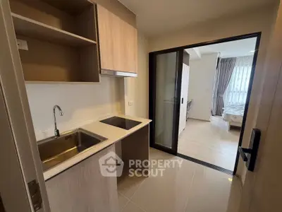 Modern compact kitchen with open layout leading to a cozy bedroom, featuring sleek cabinetry and a built-in cooktop.