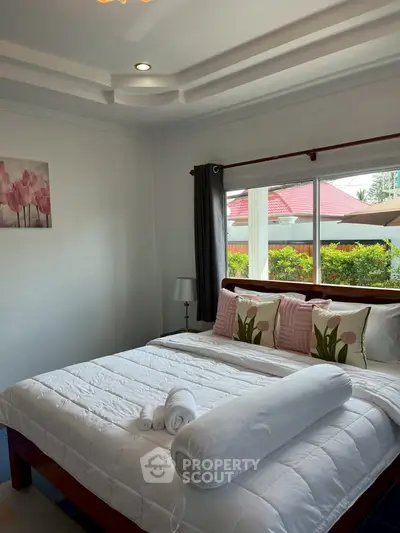 Cozy bedroom with large window and garden view, featuring elegant decor and plush bedding.