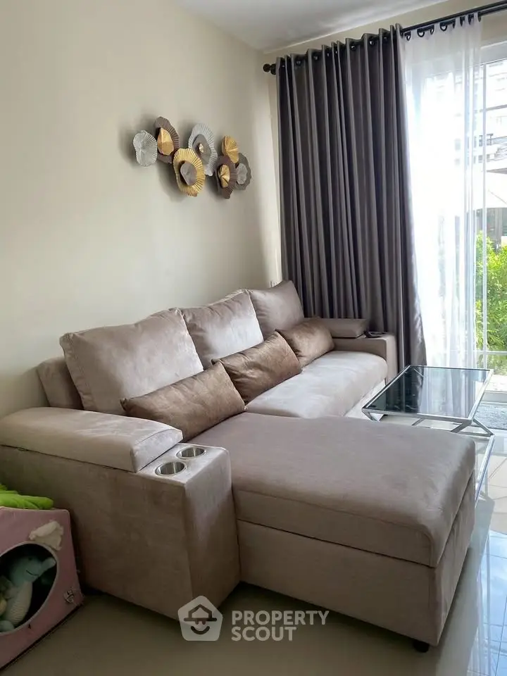 Cozy living room with plush beige sofa and glass coffee table, featuring elegant wall decor and floor-to-ceiling curtains.