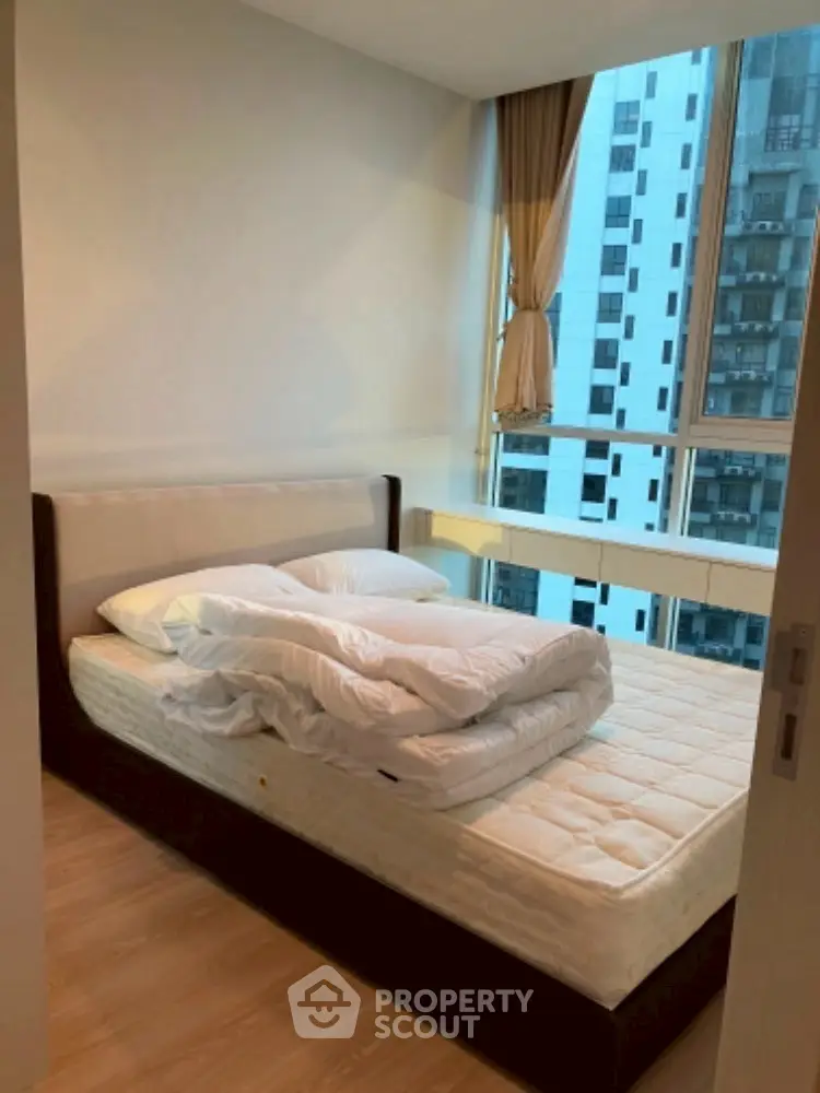 Cozy bedroom with large window offering city view in modern apartment.