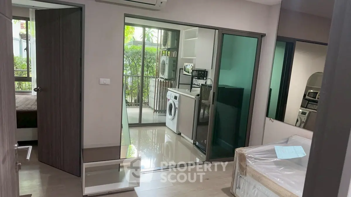 Modern apartment interior with glass partition, washing machine, and compact kitchen.