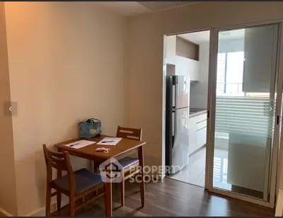 Cozy dining area with wooden table and chairs adjacent to modern kitchen with fridge.
