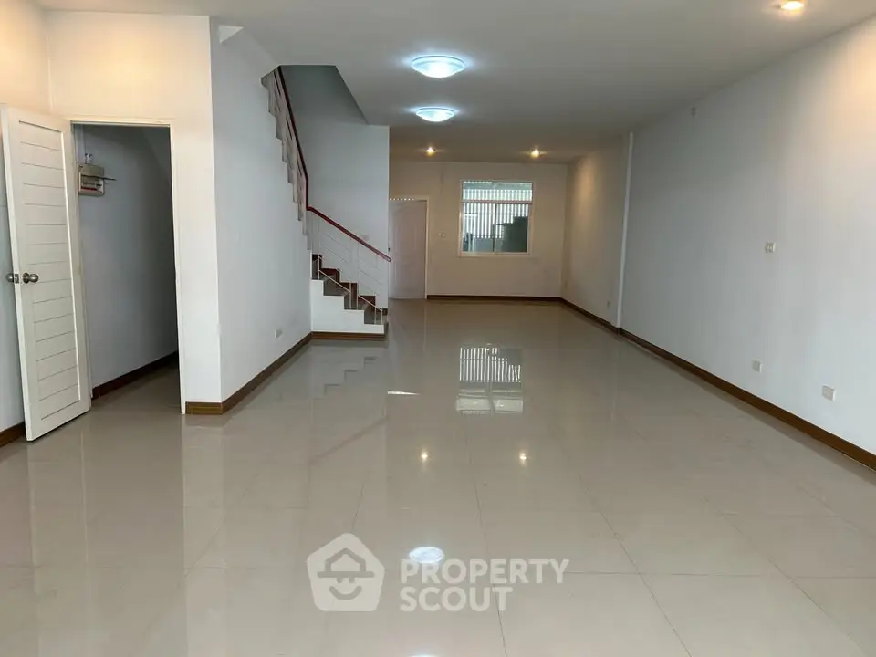 Spacious open-plan living area with glossy tiled floors and staircase, perfect for modern living.