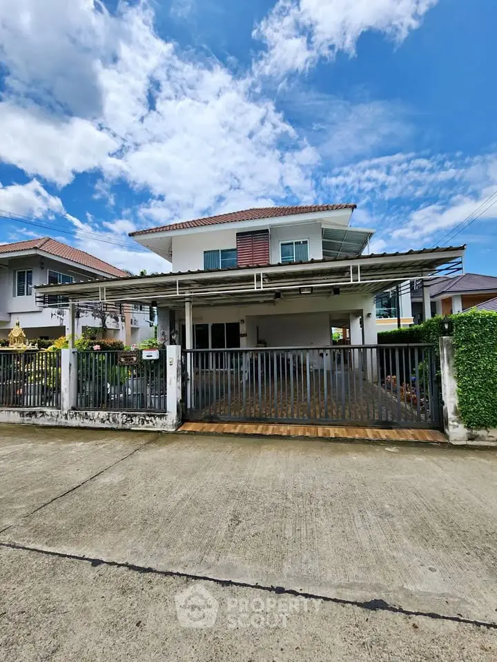 Charming two-story house with gated driveway and lush greenery under a bright blue sky.