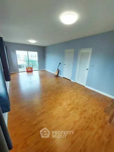 Spacious living room with wooden flooring and balcony access, perfect for relaxation and entertainment.