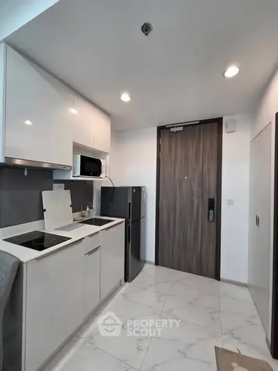 Modern compact kitchen with sleek white cabinets and built-in appliances in a stylish apartment.