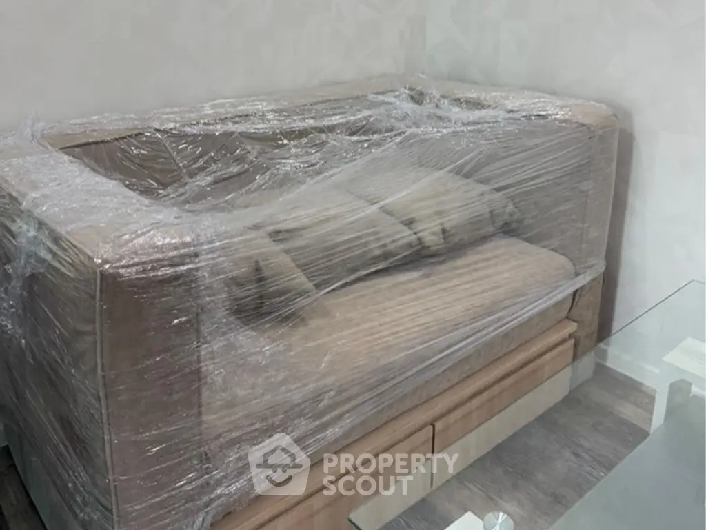 Modern living room with wrapped sofa and glass table, ready for move-in.