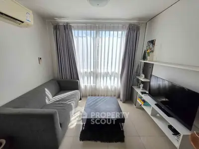 Cozy living room with modern gray sofa, TV, and large window with curtains.