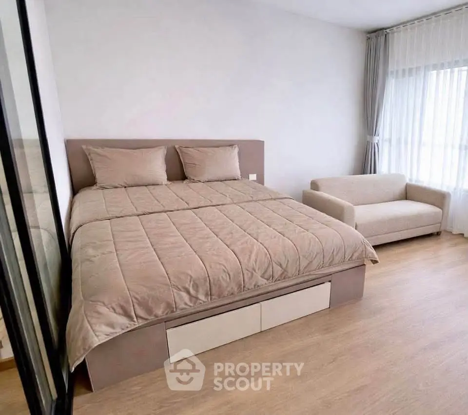 Spacious bedroom with cozy bed and sofa, featuring large windows for natural light.