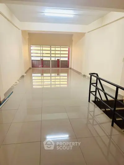 Spacious open-plan room with glossy tiled floors and large windows, ideal for versatile living or office space.