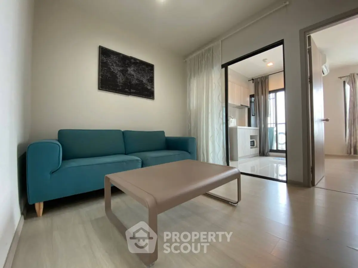 Modern living room with teal sofa and sleek coffee table, open layout to kitchen area.