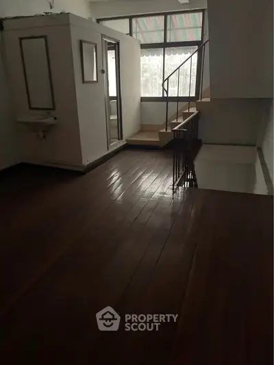 Spacious interior with wooden flooring and large windows, featuring a unique staircase design.