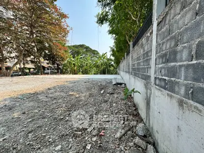 Vacant land with potential for development, featuring a boundary wall and lush greenery in the background.