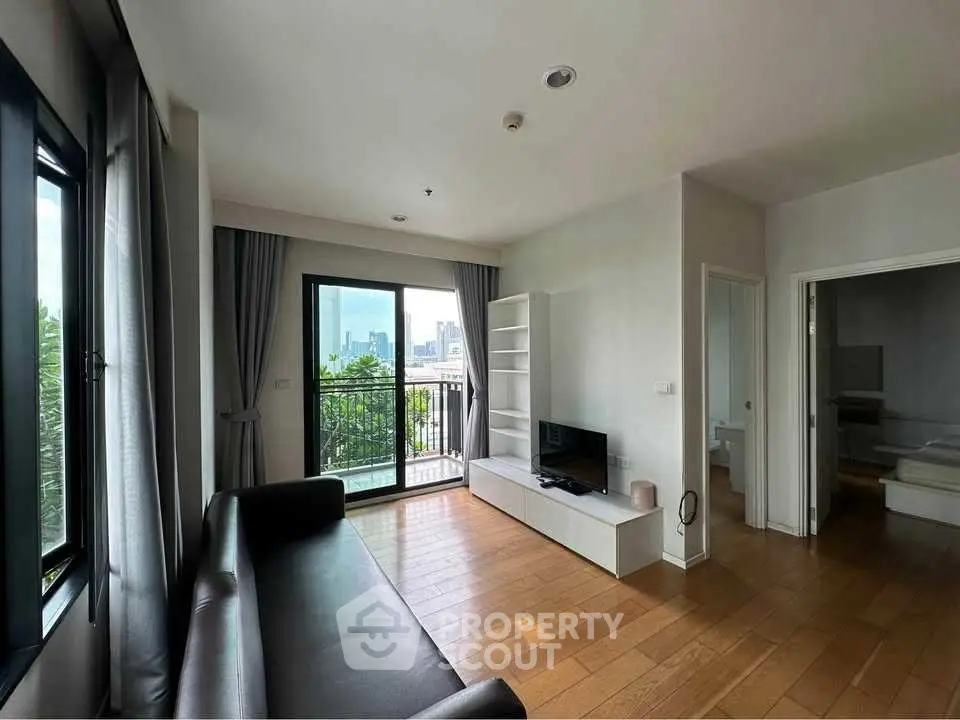 Modern living room with balcony and city view, featuring sleek furniture and wooden flooring.