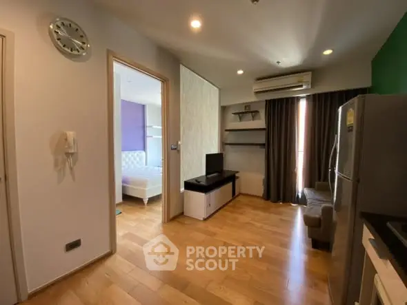Modern apartment interior with wooden flooring, open living area, and visible bedroom.