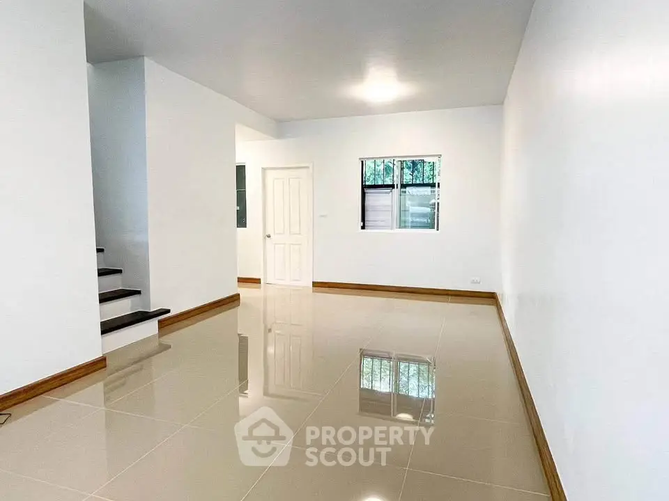 Spacious modern living room with glossy tiled floors and staircase in a minimalist home.