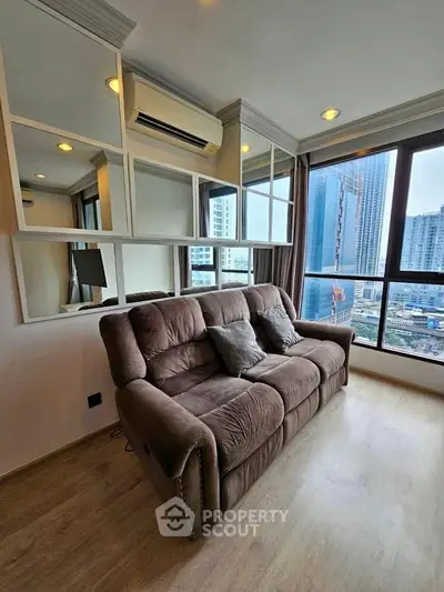 Modern living room with plush sofa and city view, featuring mirrored wall accents and natural light.