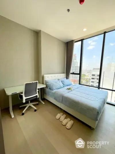 Modern bedroom with city view, featuring a comfortable bed and study desk, ideal for urban living.