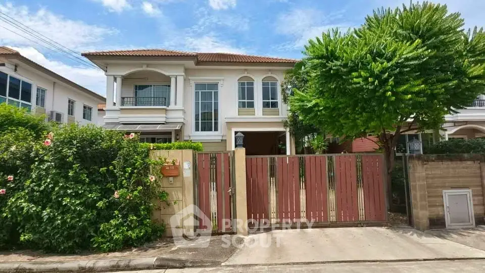 Charming two-story house with lush greenery and gated entrance in a serene neighborhood.
