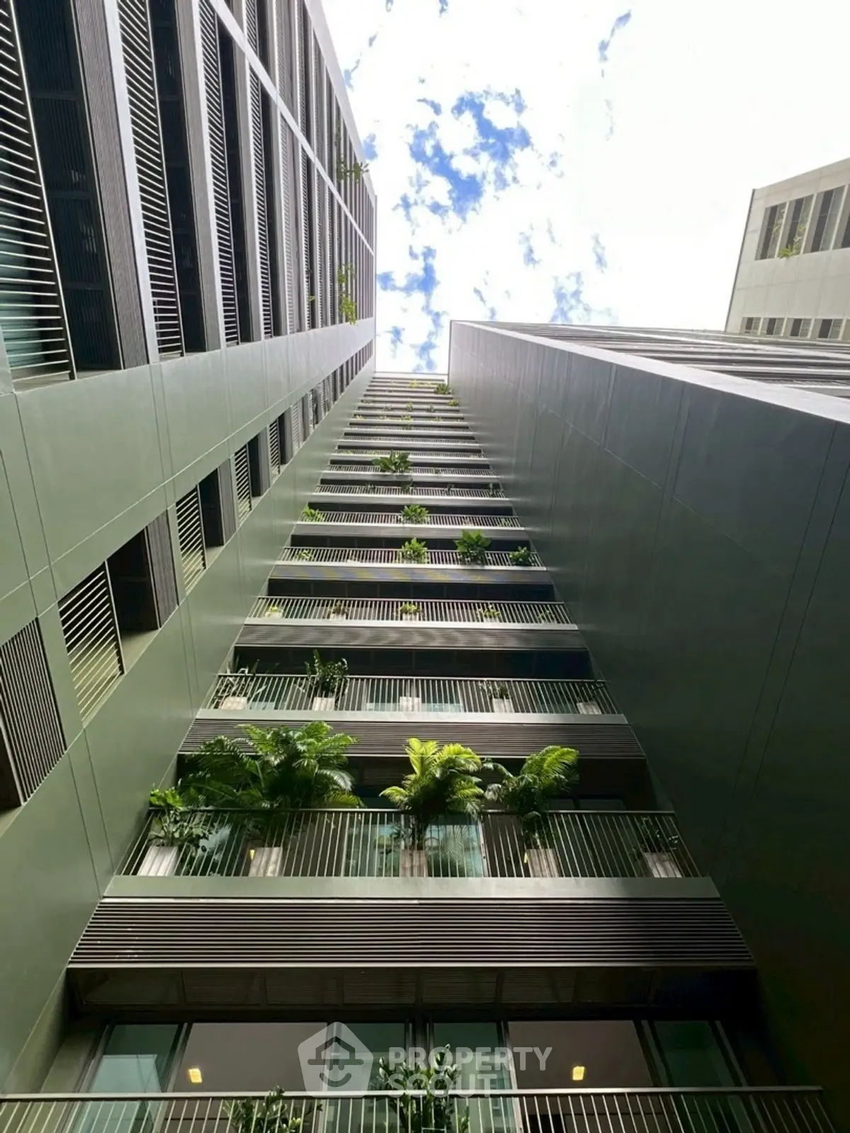 Modern high-rise building with lush green balconies and clear sky view.