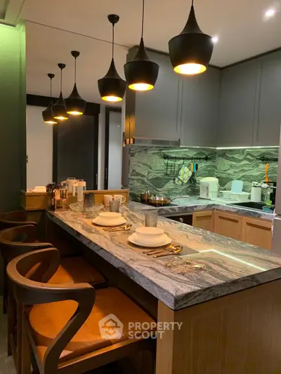 Modern kitchen with elegant lighting and marble countertop, featuring stylish bar seating and sleek cabinetry.
