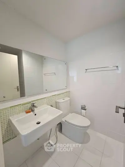 Modern bathroom with white tiles and sleek fixtures, featuring a wall-mounted sink and toilet.