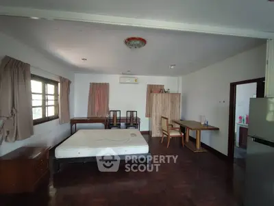 Spacious bedroom with wooden flooring and natural light, featuring a bed and dining area.
