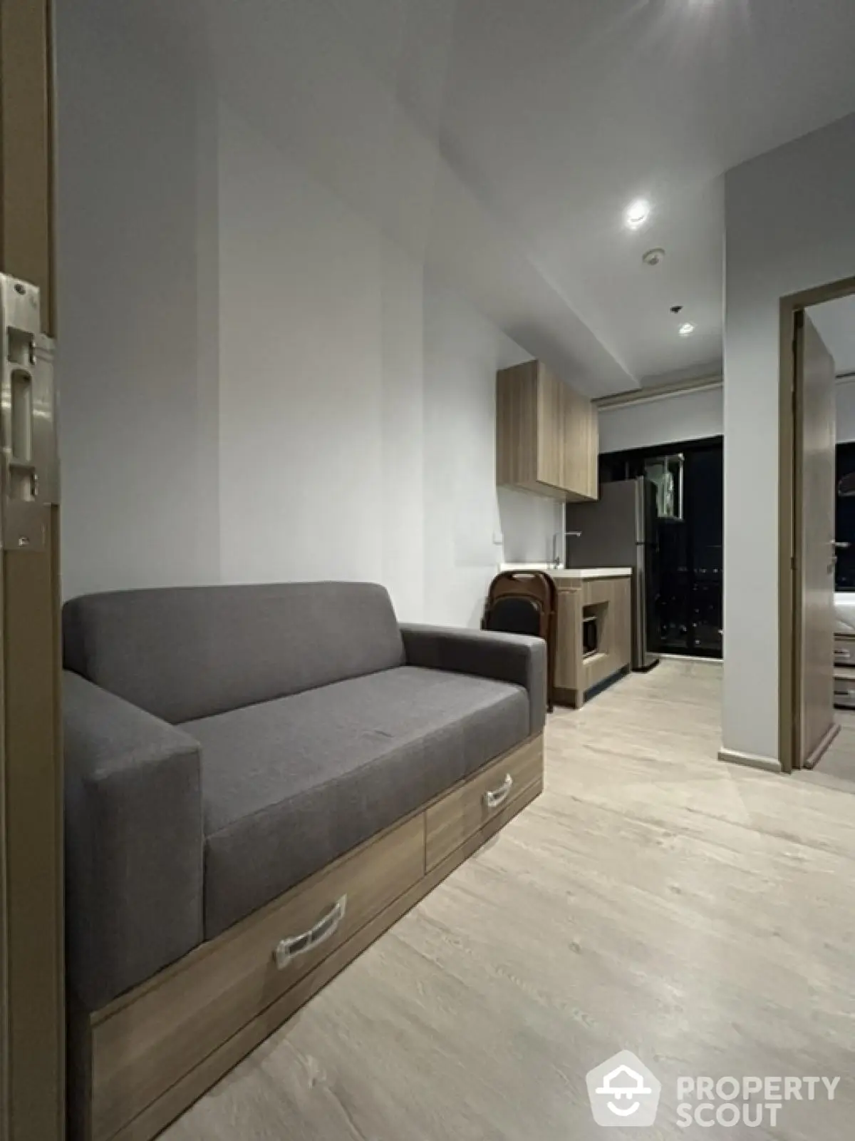 Modern apartment interior with sleek gray sofa and compact kitchen area.