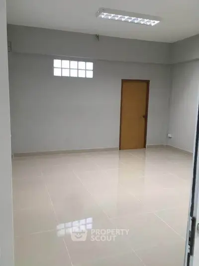 Spacious empty room with tiled flooring and wooden door, ideal for customization.