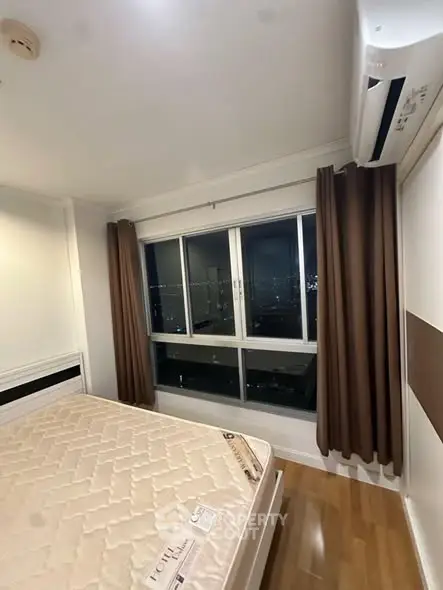 Modern bedroom with city view, featuring large window and air conditioning unit.