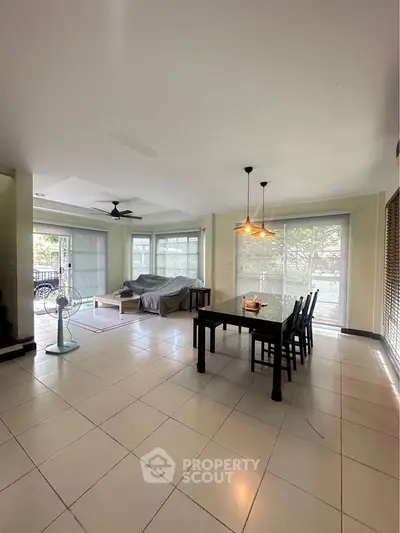 Spacious living room with large windows and modern dining area in a bright, airy apartment.