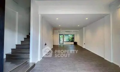 Spacious open-plan living area with modern staircase and large window view.