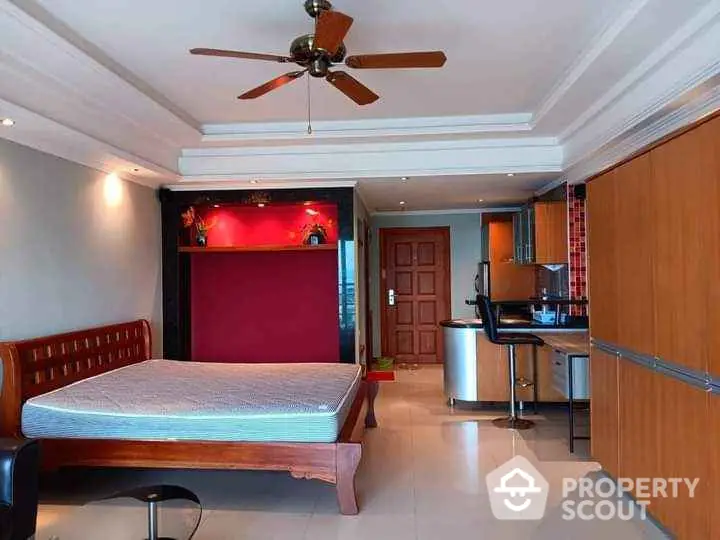 Spacious bedroom with modern kitchen and ceiling fan in open layout apartment.