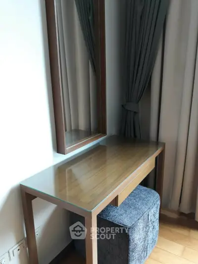 Elegant wooden vanity table with mirror and plush stool in a modern bedroom setting.
