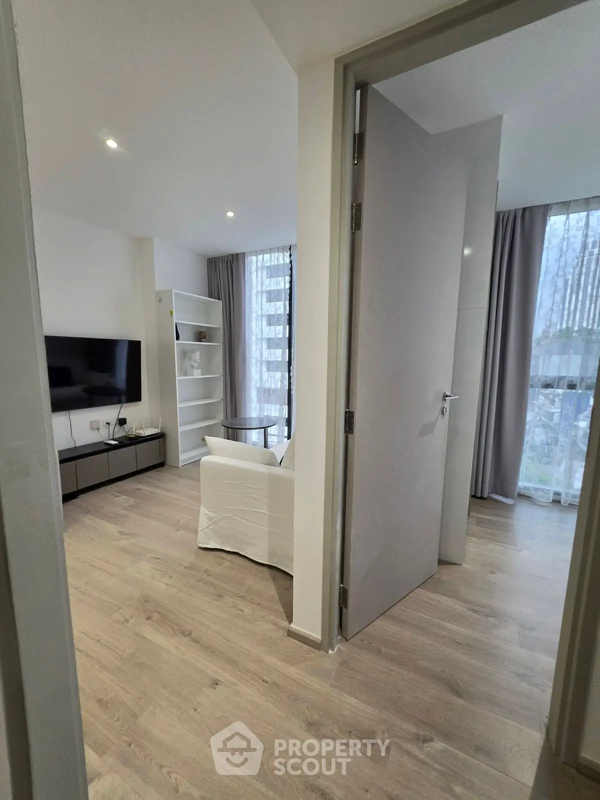 Modern living room with sleek design and natural light, featuring a wall-mounted TV and stylish furniture.