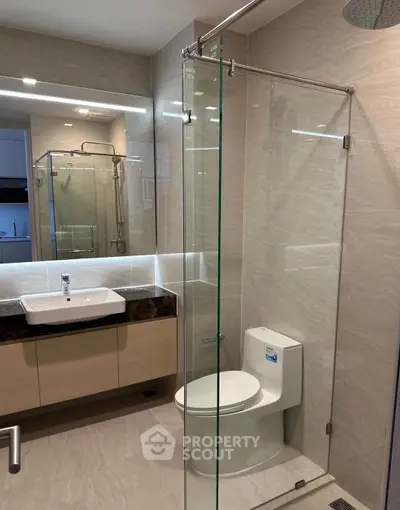 Modern bathroom with glass shower, sleek vanity, and elegant fixtures in a contemporary apartment.