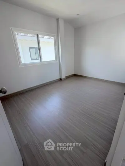 Spacious empty bedroom with large window and modern flooring, perfect for customization.