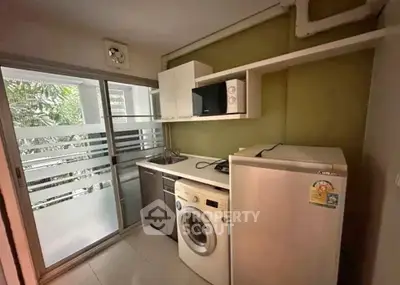 Compact kitchen with washing machine and microwave, featuring a sliding glass door to a balcony.