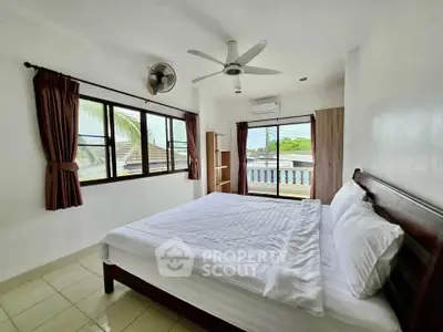 Spacious bedroom with large windows and ceiling fan, offering a bright and airy atmosphere.
