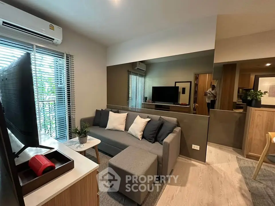 Modern living room with stylish decor and natural light, featuring a cozy gray sofa and sleek TV setup.