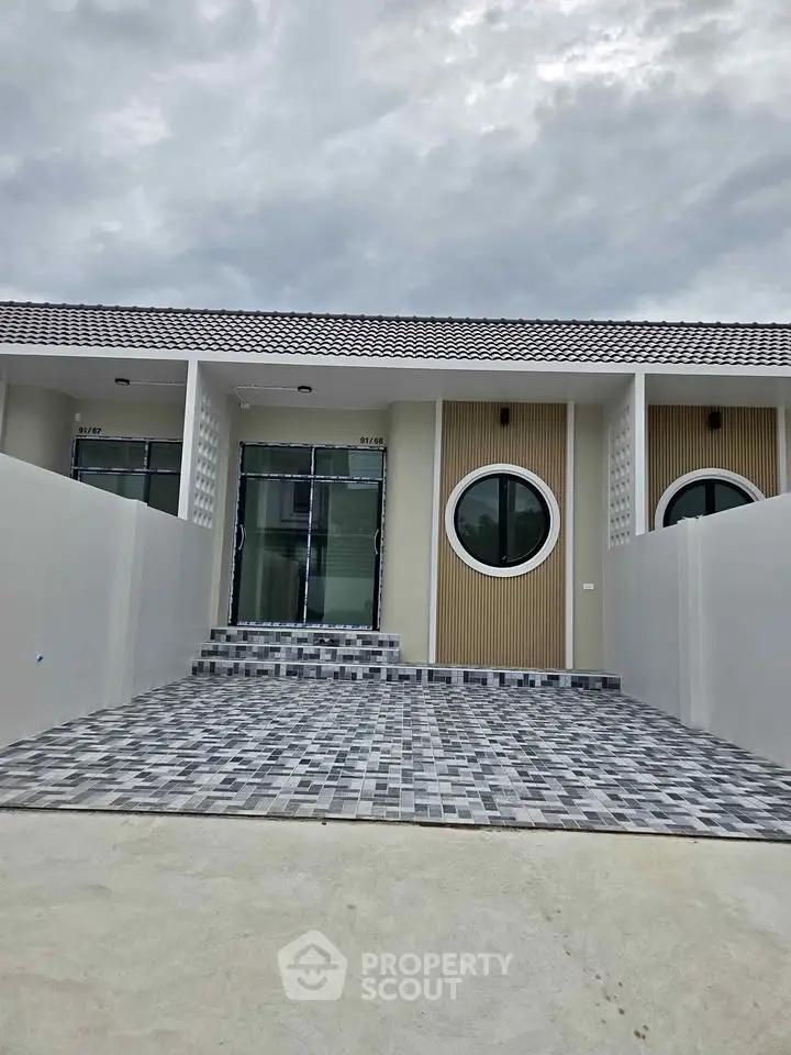Modern single-story house with unique circular windows and stylish tiled driveway.