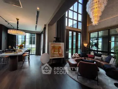 Luxurious modern living room with high ceilings, elegant chandeliers, and large windows offering natural light.