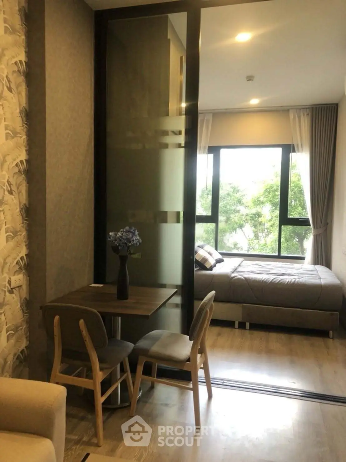 Modern studio apartment with cozy bedroom and dining area, featuring large windows and stylish decor.