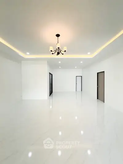 Spacious modern living room with elegant chandelier and sleek white flooring.