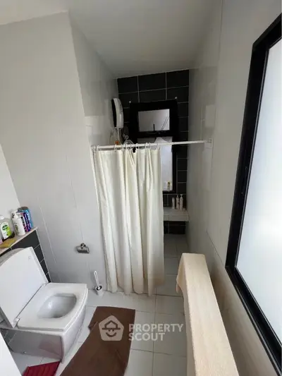 Modern bathroom with sleek tiles and natural light, featuring a shower curtain and essential amenities.