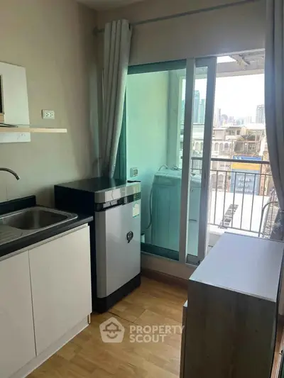 Modern apartment kitchen with balcony and city view, featuring sleek cabinetry and washing machine.