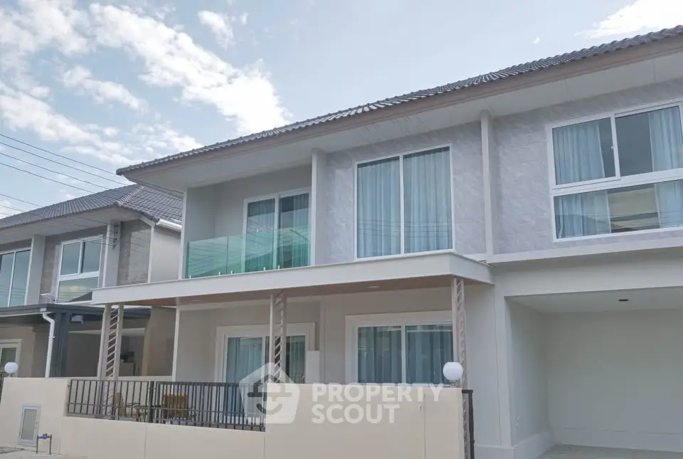 Modern two-story house with large windows and balcony in a serene neighborhood.