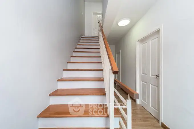 Modern staircase with wooden steps and white railing in a bright hallway